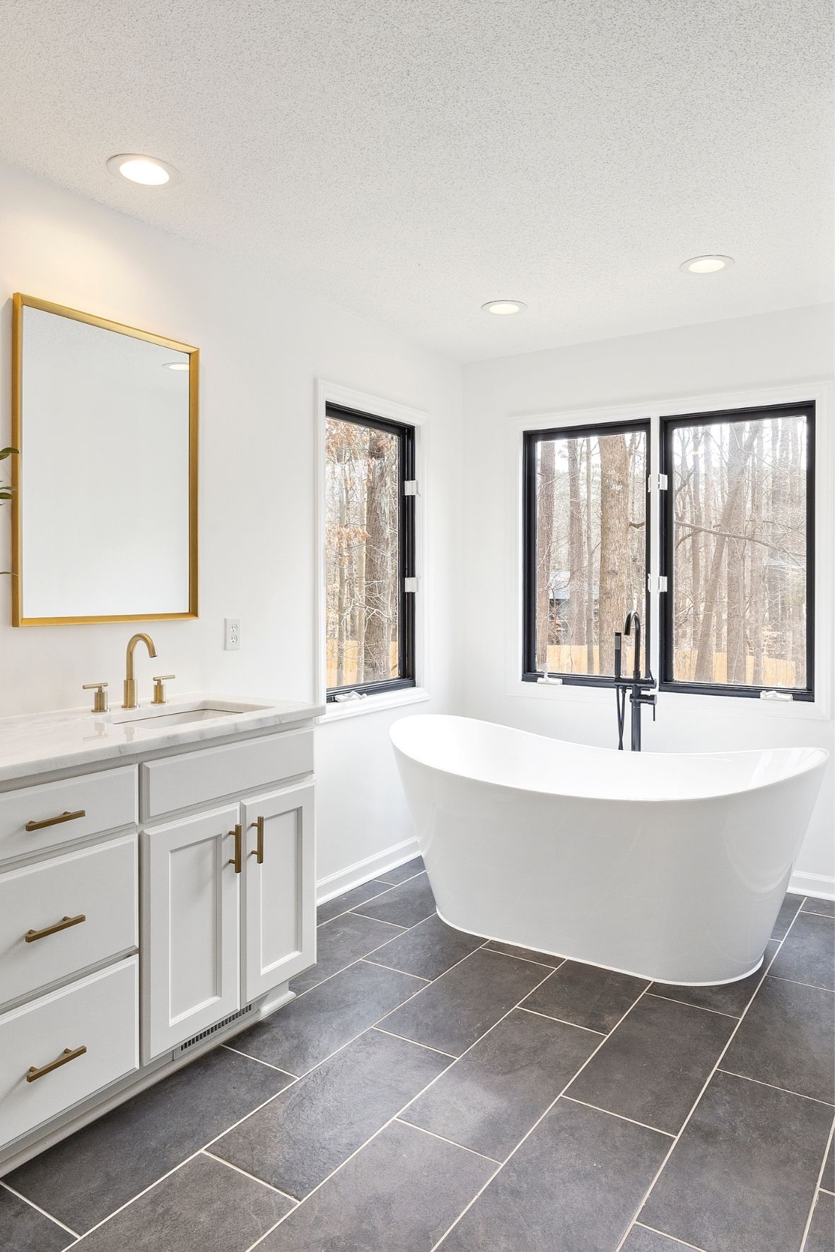 Salle de bain lumineuse avec baignoire autoportante, meuble blanc et grandes fenêtres au cadre foncé  à Montréal