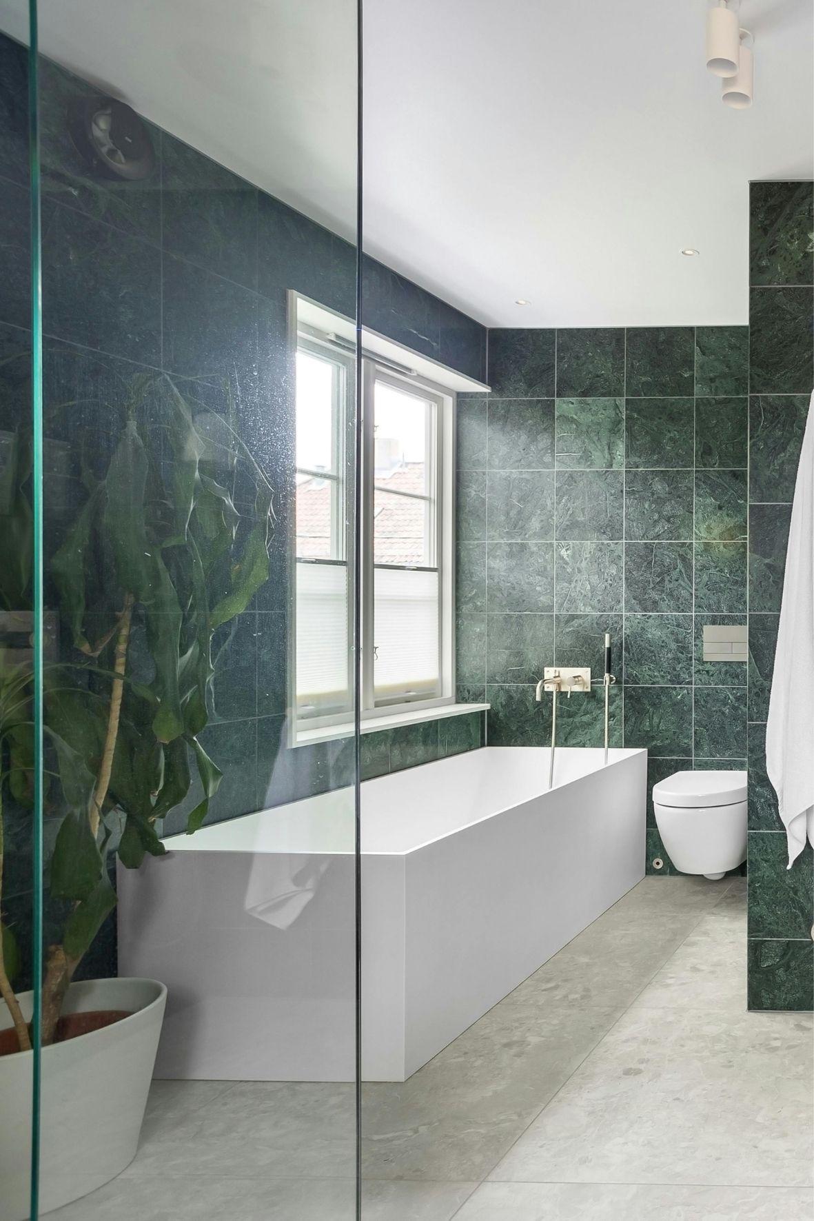 Salle de bain avec baignoire encastrée, WC suspendu, murs carrelés verts et sol clair à Saint-Eustache